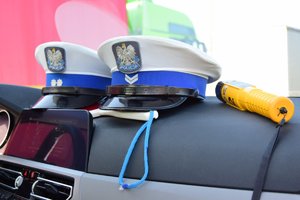 Na zdjęciu widoczna deska rozdzielcza samochodu, na której położone są czapki policyjne i urządzenie Alcoblow w kolorze żółtym służące do badania stanu trzeżwiści