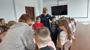 spotkanie policjantów z dziećmi przedszkola nr 13 z Przemyśla. Dzieci stoją przy policjantce i omawiają elementy wyposażenia i umundurowania