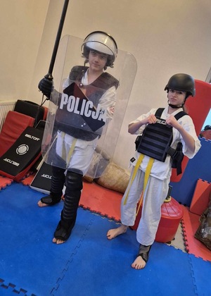 spotkanie policjantów z dziećmi ze szkoły karate w Przemyślu. uczniowie ubrani w kimona mają ubrane elementy wyposażenia umundurowani policjantów.