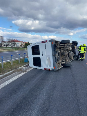 Zdarzenie drogowe w m. Hurko, na drodze leży przewrócony na lewy bok bus koloru białego . Obok stoją strażacy.