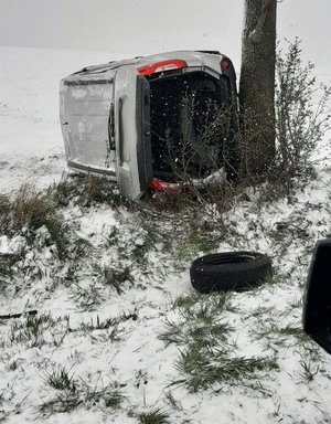 zdjęcie przedstawia białego busa, przewróconego na prawy bok. samochód znajduje się na przydrożnym polu.