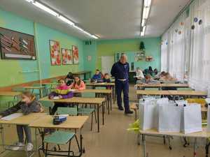 zdjęcia przedstawiają dzieci reprezentujące szkoły podstawowe podczas turnieju. młodzież siedzi w ławkach szkolnych i pisze test z wiedzy o ruchu drogowym.