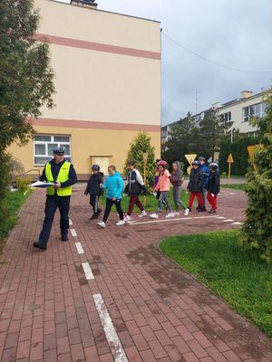 zdjęcia przedstawiają dzieci reprezentujące szkoły podstawowe podczas turnieju. umundurowany policjant prowadzi dzieci na plac szkolny. pierwszy idzie policjant za nim dzieci