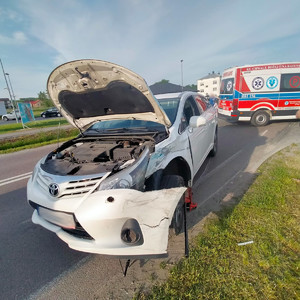 biały samochód z uszkodzonym przednią lewa częścią. zderzak samochodu częściowo oderwany