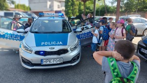 zdjęcia przedstawiają grupę uczestników półkolonii podczas spotkania na terenie Komendy Miejskiej Policji w Przemyślu. dzieci podczas oglądania radiowozu policyjnego oznakowanego