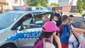 zdjęcia przedstawiają grupę uczestników półkolonii podczas spotkania na terenie Komendy Miejskiej Policji w Przemyślu. dzieci podczas oglądania radiowozu policyjnego oznakowanego