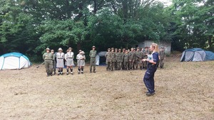 na zdjęciu harcerze podczas prelekcji policjantki stoją w dwuszeregu na polu namiotowym