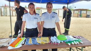 na plaży umundurowane policjantki stoją przy stoliku na którym znajdują się materiały promocyjne