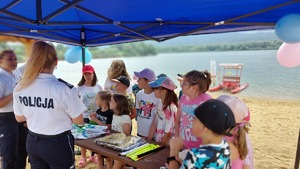 policjantki prowadzą rozmowę z dziećmi w tle widać plażę i  jezioro