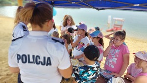 policjantki w trakcie prelekcji z dziećmi , w tle plaża i zalew