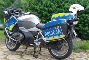 motocykl policyjny w kolorze srebrno czarnym z umieszczonymi bagażnikami na jego tylnej części ,na których widnieje napis policja