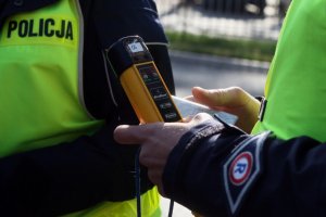 Policjant umundurowany trzymający w ręce urządzenie do badani stanu trzeźwości w kolorze żółtym .