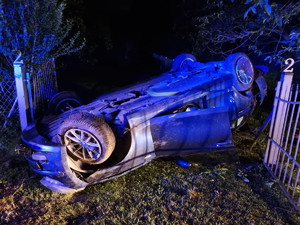 Pojazd bmw lezący na dachu koło ogrodzenia