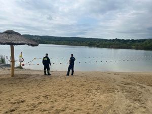 policjant i strażak na plaży w ostrowie, w tle widoczny akwen